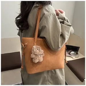 Detail of a large brown suede tote bag featuring a plush bear charm and side drawstring