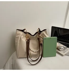 Detail of cream tote bag featuring pearl charm, gold chain, and spacious interior capacity