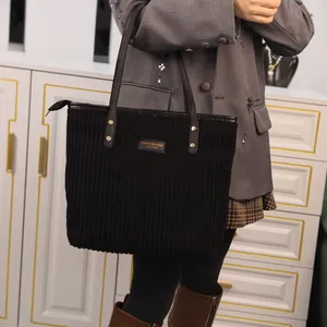 Minimalist black corduroy tote bag with leather straps and gold metal plaque