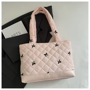 Detail of light pink quilted tote bag with black bow embroidery and leather base