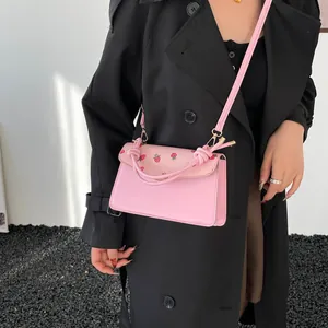 Pink floral crossbody bag with strawberry print and decorative knot handles on black coat