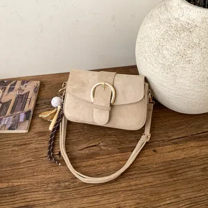 Detail of light khaki suede crossbody bag with large golden buckle and baseball charm