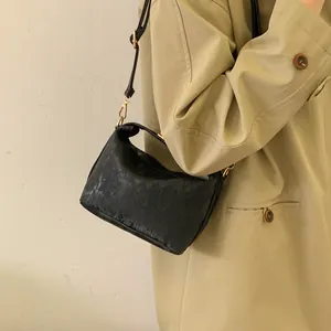 Detail of a textured black crossbody bag with gold hardware worn over a khaki trench coat