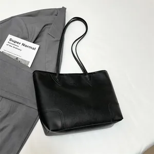 Detail of black lychee grain leather tote bag with reinforced stitching on gray blazer