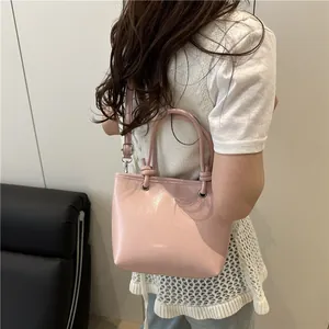 Sac seau rose brillant en cuir verni avec poignées rondes porté par un mannequin