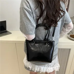 Sac seau noir brillant minimaliste avec poignées cylindriques et bandoulière réglable