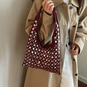 Détail du sac hobo en cuir verni rouge foncé avec rivets argentés sur l'épaule