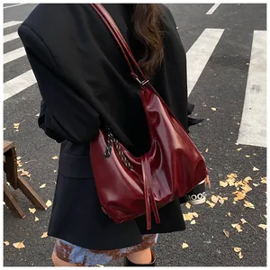 Detail einer dunkelroten Halbmond-Schultertasche aus glänzendem Leder am Modell im Freien