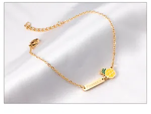 Gros plan du bracelet doré avec breloque ananas et barre gravée sur de la soie