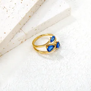 Elegant gold bypass ring featuring three blue pear-cut stones on a white textured background
