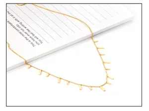 Detail of a minimalist gold necklace with rectangular bar pendants on a notebook