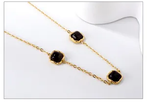 Macro view of a gold chain necklace featuring three square black stone pendants on a white base
