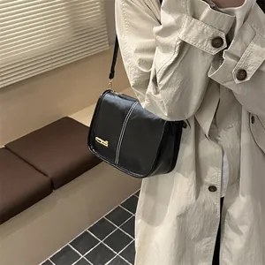 Sac fourre-tout noir chic avec coutures blanches et logo doré sur un trench beige