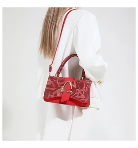 Détail du sac rouge en cuir avec boucle dorée en D porté sur un tailleur blanc