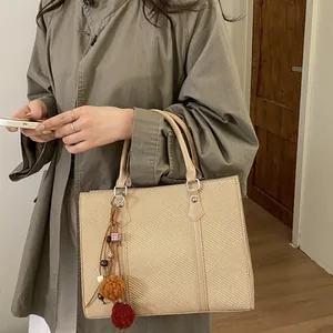 Minimalist beige woven tote bag with leather trim and decorative charm on shoulder