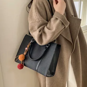 Detail of black textured tote bag with orange plush charm on brown wool coat