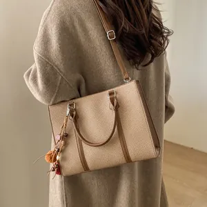 Detail view of khaki woven tote bag with brown leather trim and colorful bead charm