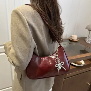 Polished wine red shoulder bag with silver bow charm worn by a model in casual attire