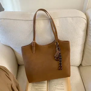Détail du sac cabas en cuir marron avec boucle en métal et breloque boulier sur sofa