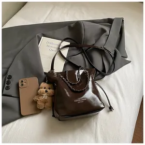Detail of glossy brown drawstring bucket bag with chain strap and teddy bear charm