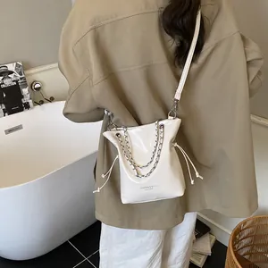 Minimalist white leather bucket bag with silver chain detail and drawstring closure