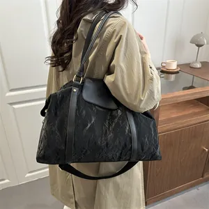 Large black crinkled travel handbag with adjustable strap shown on model's shoulder