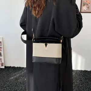 Chic two-tone crossbody bag with gold V-buckle accent on a black trench coat model