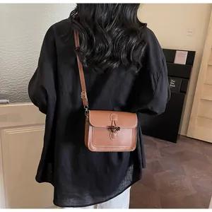 Brown leather crossbody bag with white stitching shown on a model in a cozy indoor setting