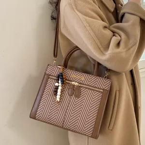 Detalle del bolso bandolera con diseño de espiga, ribete de cuero marrón y dije de cuentas