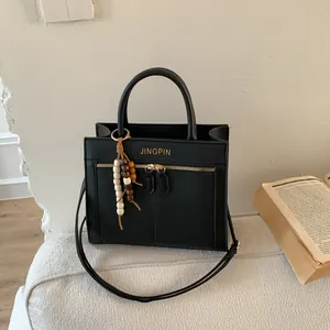 Detalle de bolso bandolera de cuero granulado negro con texto dorado y colgante de cuentas