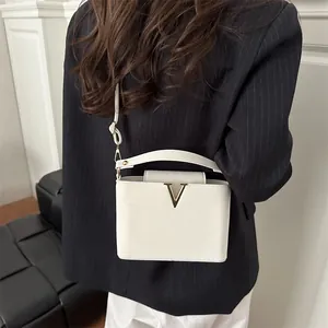 White large capacity square crossbody bag with gold V clasp on model in suit