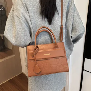 Detail of a brown crocodile pattern handbag with gold lettering on a casual outfit