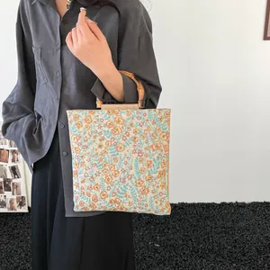 Floral canvas tote bag with natural bamboo handles held by a model in a minimalist setting