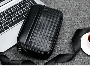 Détail d'une bandoulière en cuir tressé avec zip métallique près d'un ordinateur