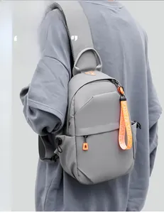 Detail of grey crossbody sling bag with orange zipper pullers on model's shoulder