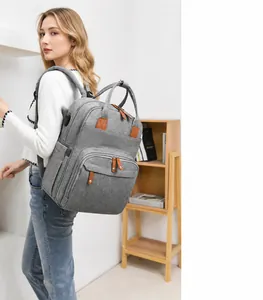 Gray multifunctional diaper backpack with USB port shown on model in a cozy room