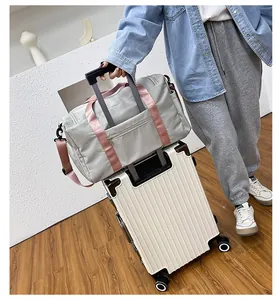 Detalle de bolsa de viaje gris con correas rosas fijada en el asa de una maleta blanca