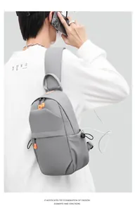 Detail of grey crossbody sling bag with USB charging port and orange zipper accents