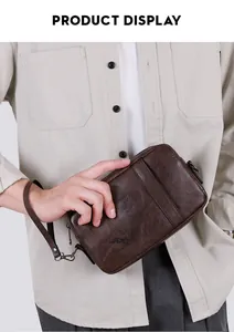 Close-up of brown leather clutch bag featuring embossed logo and detachable wrist strap