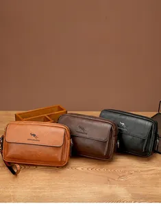 Three men's leather crossbody bags in black, dark brown, and tan on a wooden surface