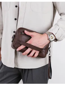 Detail of a dark brown men's clutch bag featuring a wrist strap and textured leather finish