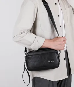 Detail of black crossbody bag showing HCDS logo, dual zippers, and adjustable strap