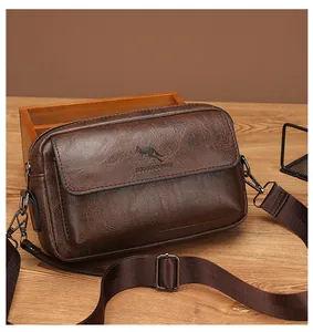 Detail of dark brown leather crossbody bag with lychee texture and metallic hardware