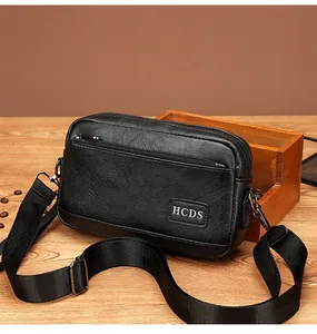 Close-up of black leather crossbody bag with dual zippers and HCDS logo on wood surface