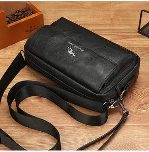 Detail view of black litchi texture cross-body bag with silver kangaroo logo on wood