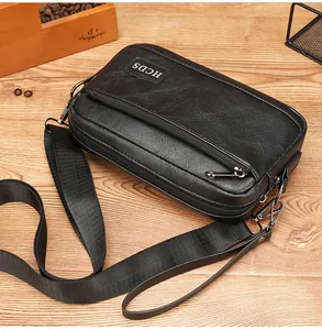 Detail of black pebbled leather crossbody bag with dual zippers on a wooden table