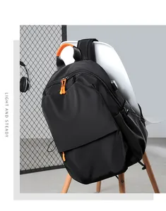 Detail of black backpack with USB charging port and orange zipper accents on white chair