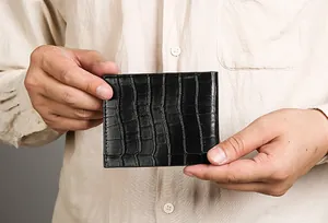 Detail of crocodile embossed leather wallet held by hand showcasing portable size