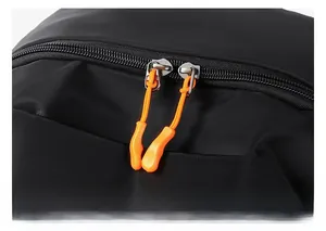 Macro shot of smooth dual metal zippers with bright orange pull tabs on a black backpack