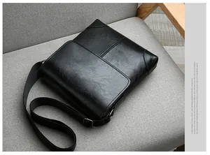 Detailed top view of black leather crossbody bag with adjustable strap on grey sofa